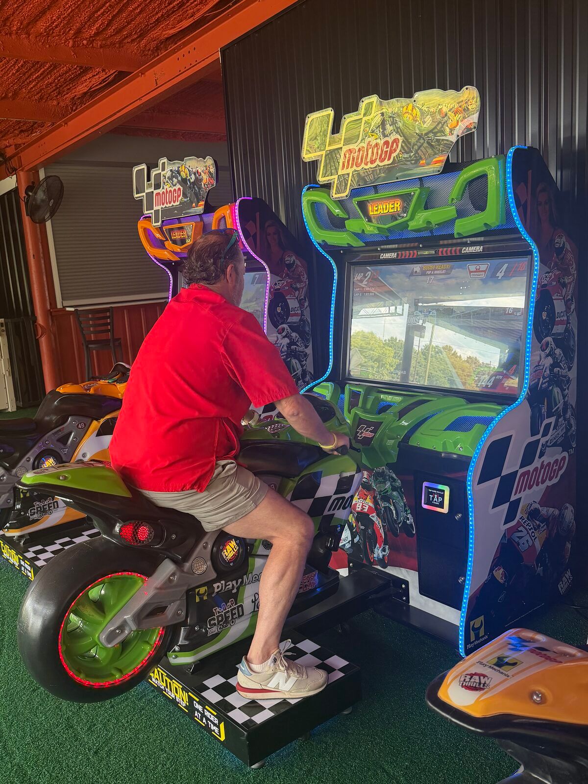 A guest riding one of the MotoGP motorcycle cabinets at Platform 32, the race running on the screen in front of him.