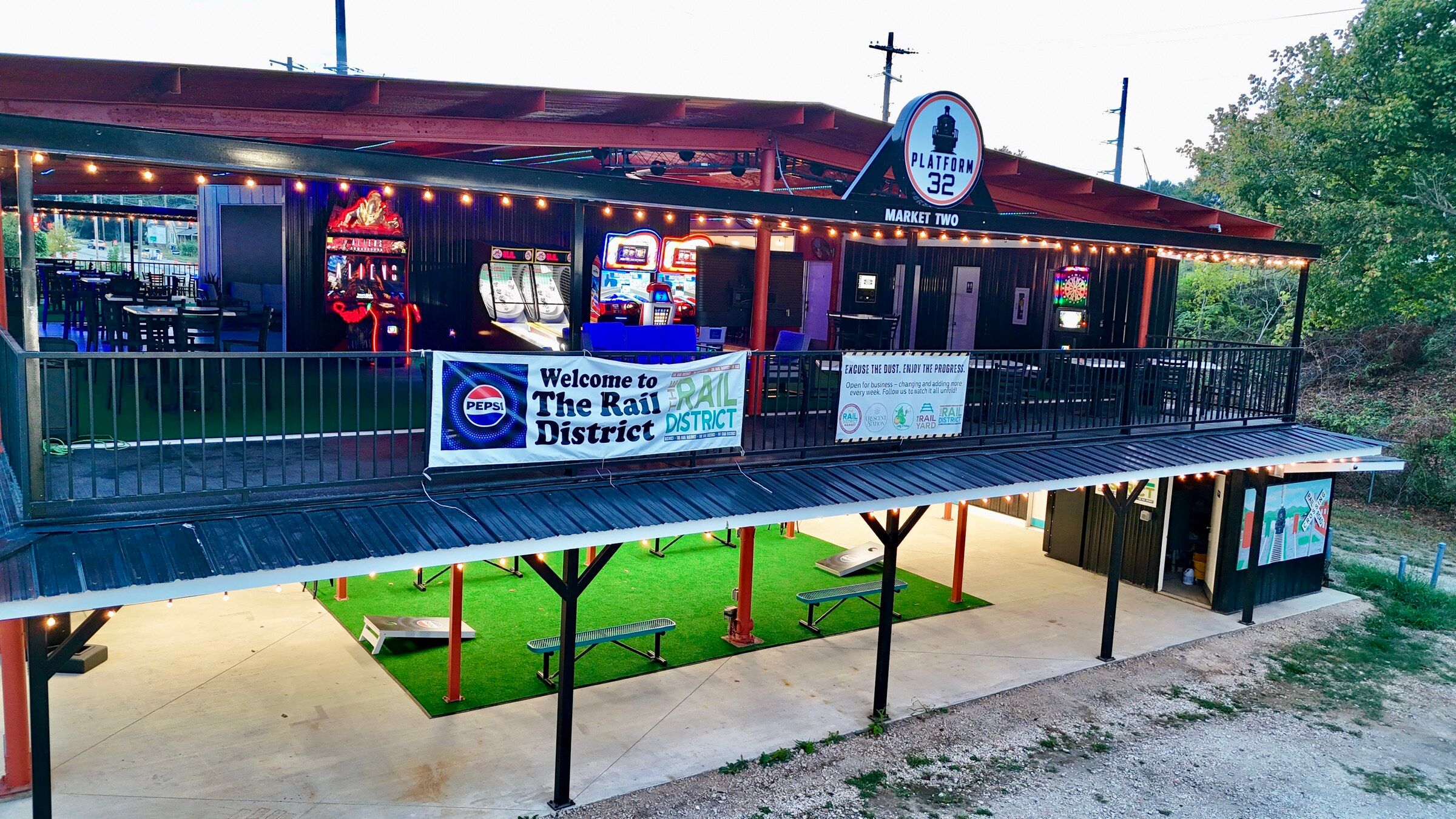 Platform 32 from above at dusk, arcade cabinets and skee-ball lanes visible through the upper deck railing
