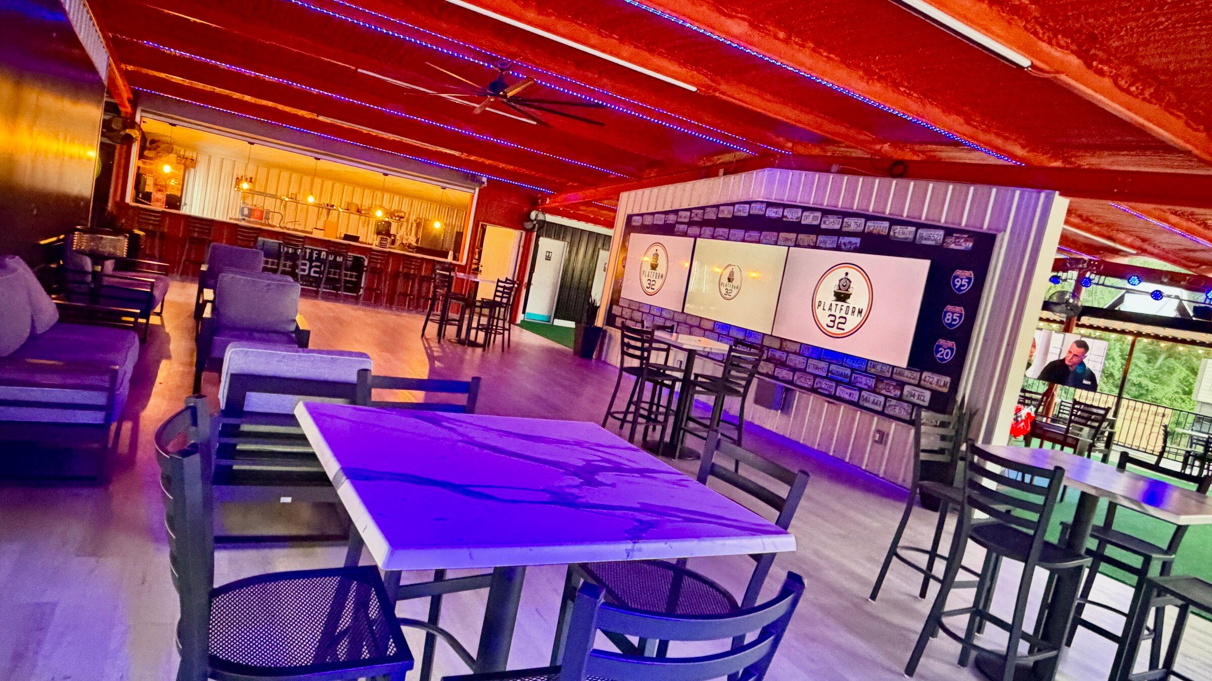 A high-top table lit purple in the Platform 32 lounge, with the bar and the licence-plate screen wall beyond
