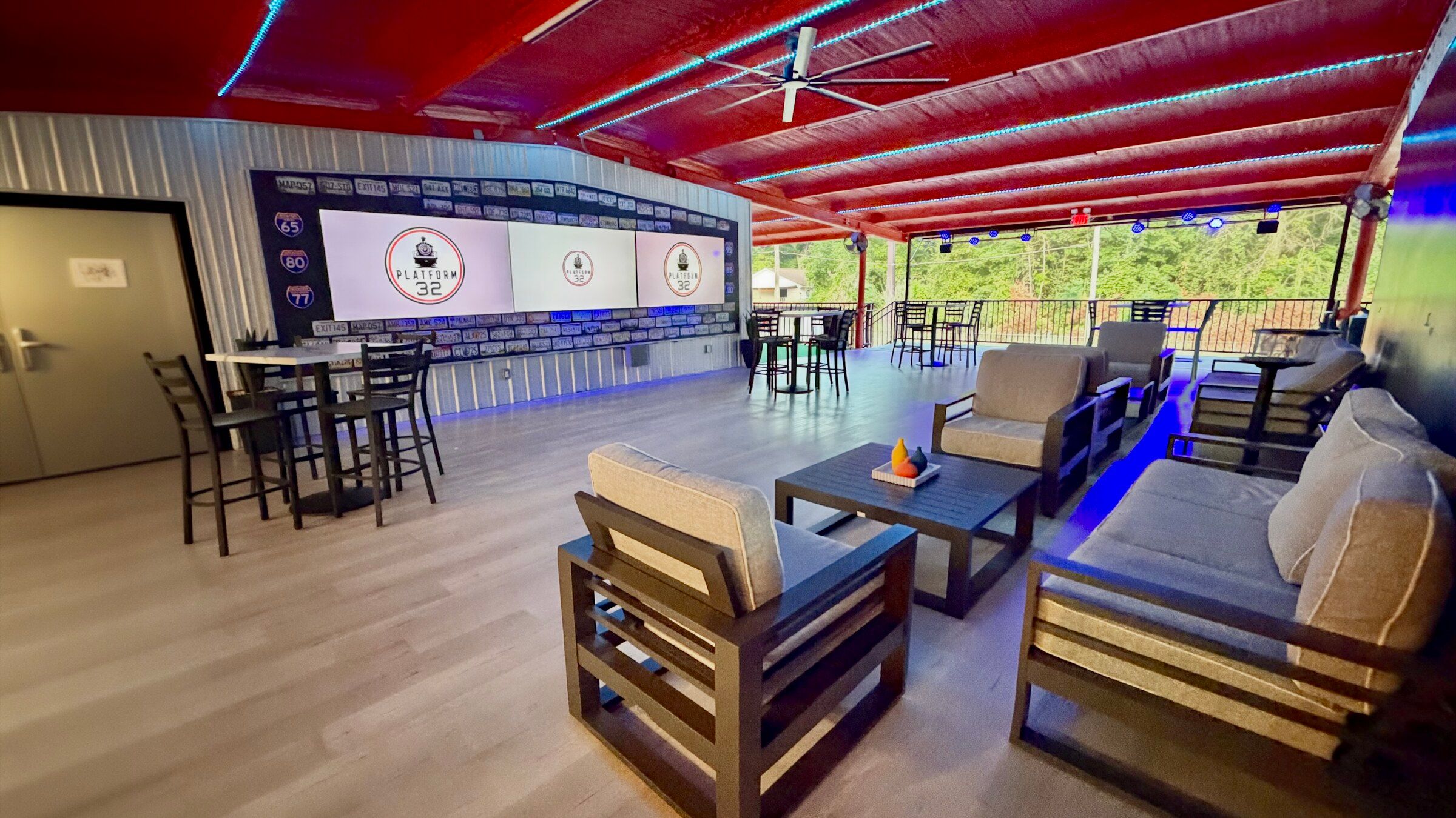 The lounge at Platform 32 at night: red ceiling, blue LED wash, and three screens on the licence-plate wall.