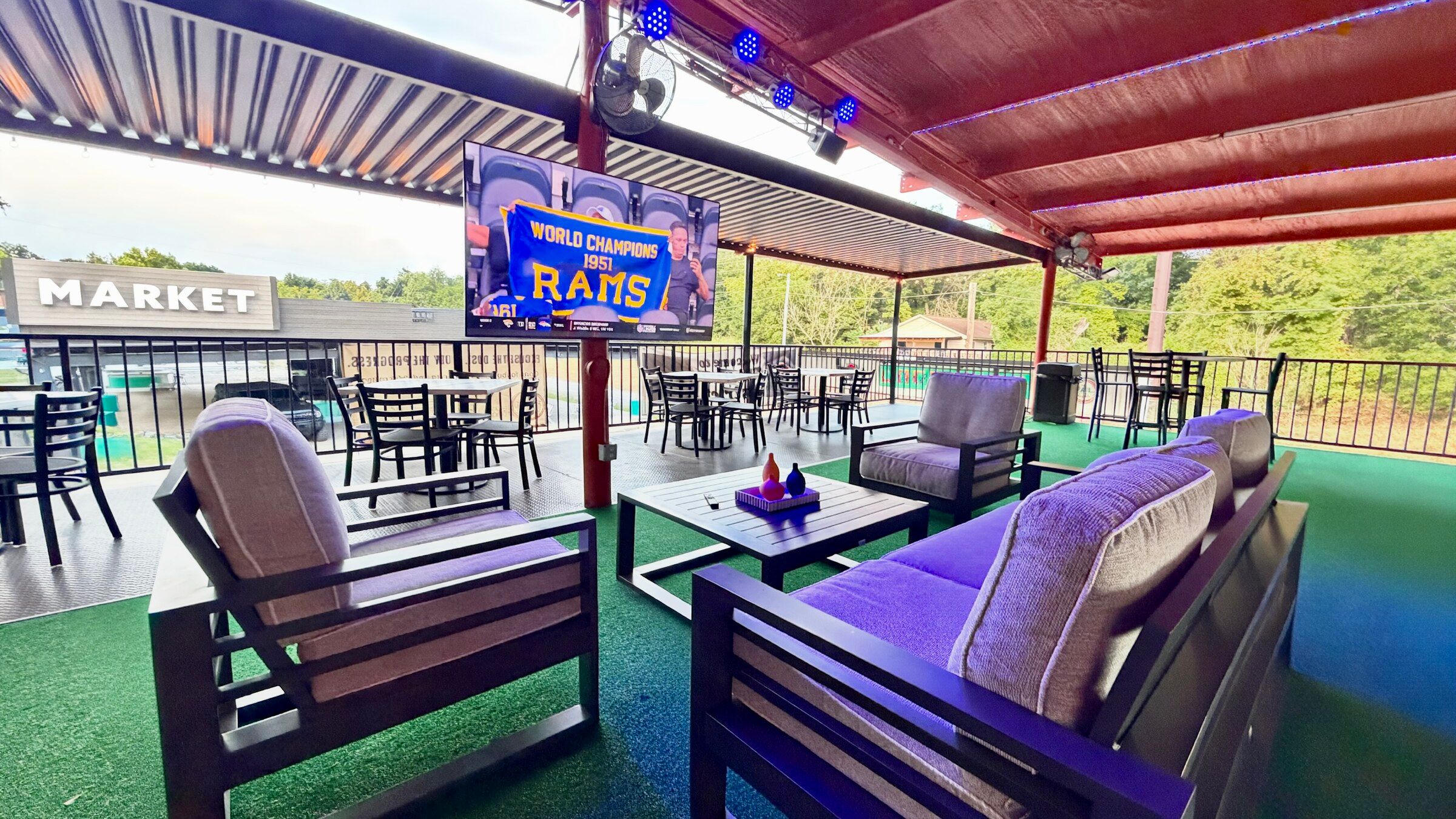 Covered patio seating at Platform 32 with a large screen showing a football broadcast and the Market building beyond